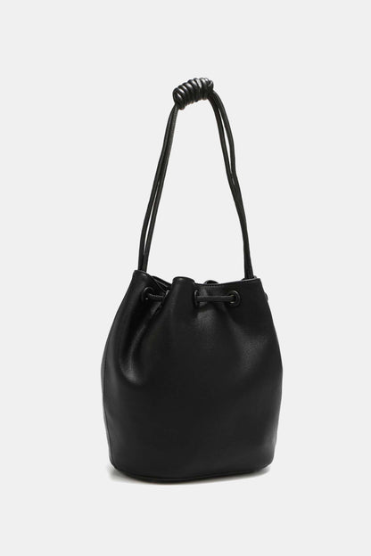 The Nicole Lee USA Amy Studded Bucket Bag by Marianela's Exclusive Shop, LLC is crafted from smooth, pebbled vegan leather with a drawstring and snap button closure. It features a handle made of two thin leather cords tied together in a knot at the top for a chic minimalist look. The bag is showcased upright against a plain white background.