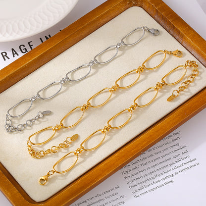 Three chain bracelets are elegantly displayed in a wooden frame. The top bracelet showcases a modern link design with silver elongated links, while the bottom two are stunning 18K gold-plated bracelets named "Gold Hollow Chain Bracelet" from Marianela's Exclusive Shop, featuring oval links and lobster clasps. A white plate and a partially visible magazine add a sophisticated touch underneath.