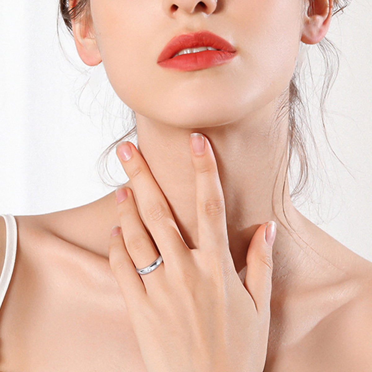 A close-up of a person with shoulder-length hair, wearing the 925 Sterling Silver Inlaid Moissanite Band Ring from Marianela's Exclusive Shop, LLC on the middle finger of their left hand. They have light skin, red lipstick, and are touching their neck with their left hand. The background is neutral.