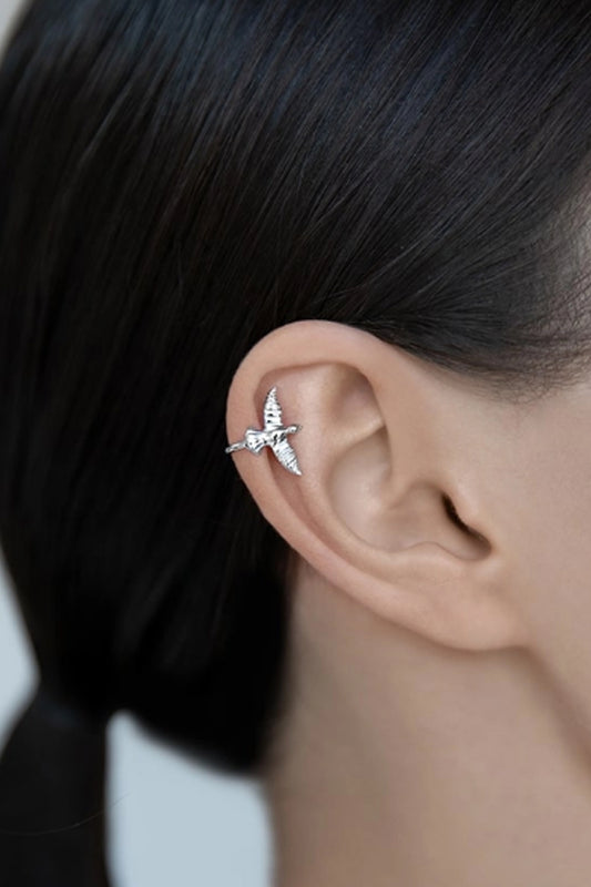 Close-up of a person's ear adorned with an adjustable, Bird-Shaped 925 Sterling Silver Single Cuff Earring by Marianela's Exclusive Shop, LLC. The person has dark hair tied back, providing a clear view of the detailed design. The background is blurred, drawing focus to the exquisite jewelry.