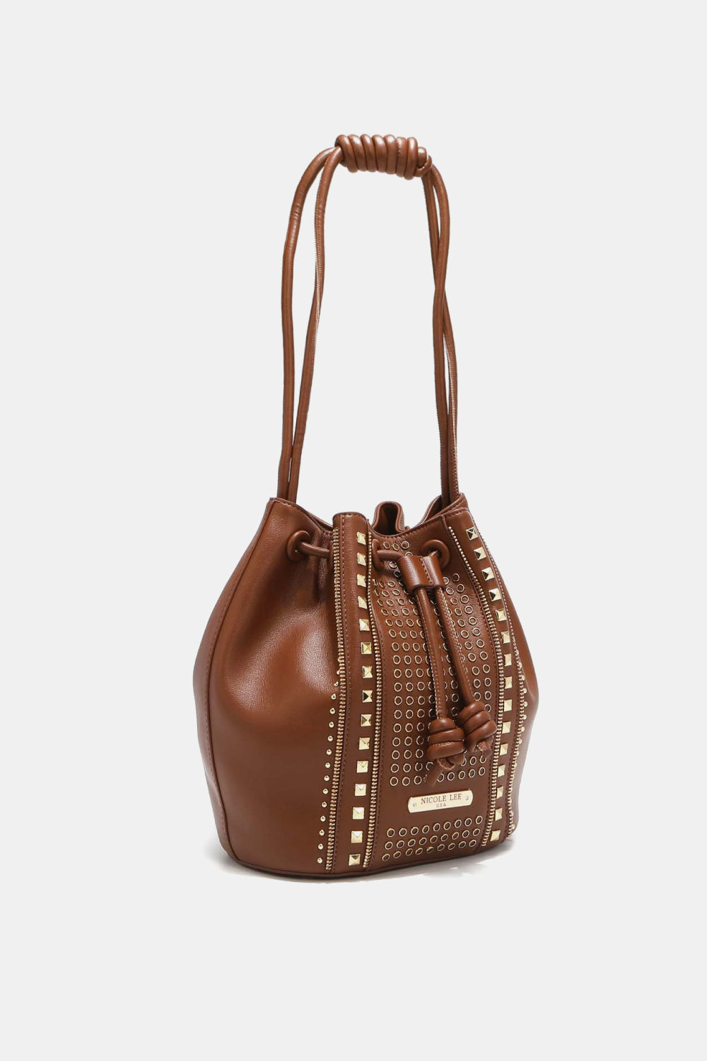 The Nicole Lee USA Amy Studded Bucket Bag from Marianela's Exclusive Shop, LLC is a brown bucket bag crafted from pebbled vegan leather and adorned with decorative gold studs and grommets in vertical patterns. It features a drawstring and snap button closure with large knots, and dual thin shoulder straps with knotted details at the top.