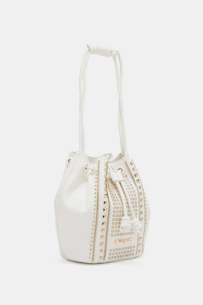 The Nicole Lee USA Amy Studded Bucket Bag from Marianela's Exclusive Shop, LLC is a white bucket bag crafted from pebbled vegan leather with gold stud detailing arranged in vertical patterns. It features a secure drawstring closure with two hanging tassels and is equipped with a knotted white strap, all set against a plain white background.