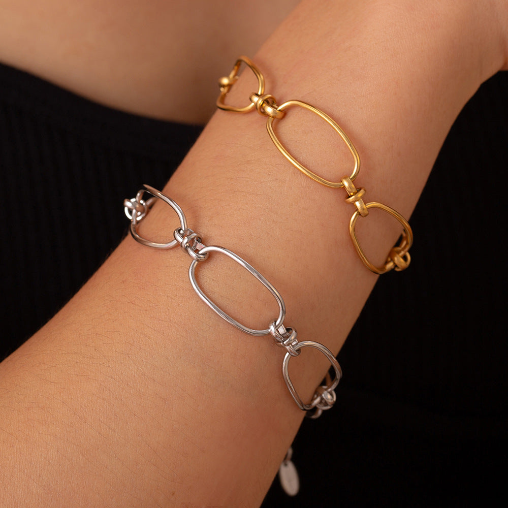 Against a dark background, a person wears two chain link bracelets on their wrist: one crafted from silver and the other, the Gold Hollow Chain Bracelet by Marianela's Exclusive Shop, is plated with 18K gold. The modern link design features oval links, highlighting a sleek and minimalistic aesthetic.