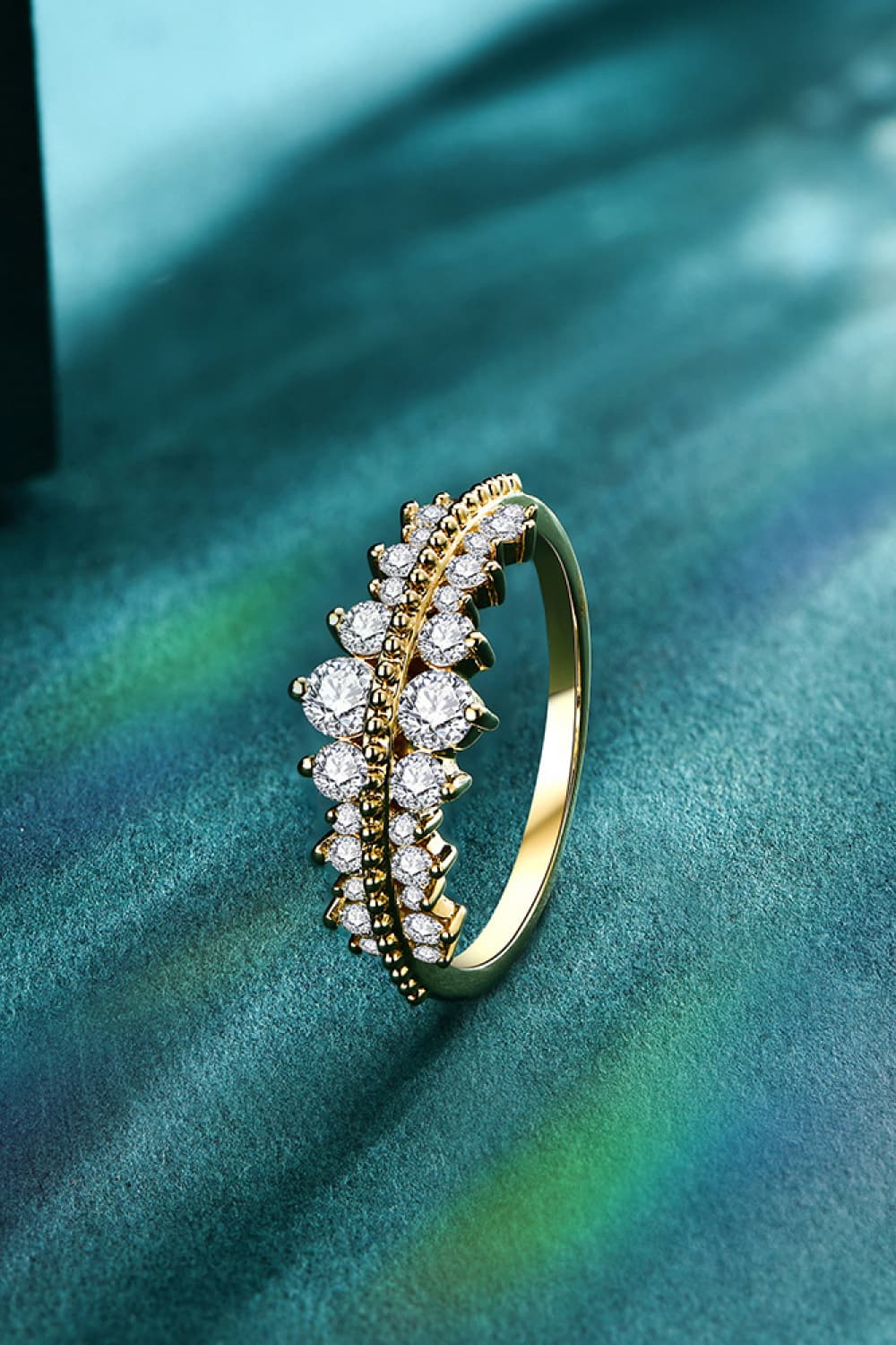 A stunning Moissanite 925 Sterling Silver Ring by Marianela's Exclusive Shop, LLC showcases a row of sparkling round stones set against a textured green surface and illuminated by beams of light.