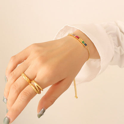 A hand with light skin tone, adorned with two rings on the index and middle fingers, and a Contrast Zircon Titanium Steel Bracelet from Marianela's Exclusive Shop, LLC. The person is wearing a white long-sleeve shirt, and the nails are painted with a gray and white gradient featuring a small decorative design.