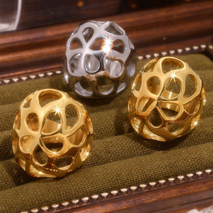 Displayed are three metallic, spherical ornaments with intricate open lattice designs: two in gold and one in silver. They rest elegantly on a textured olive green surface within a wooden frame. These pieces embody modern minimalism, akin to Marianela's Exclusive Shop's Gold-Cutout Elegance Ring, catching light and creating reflections.