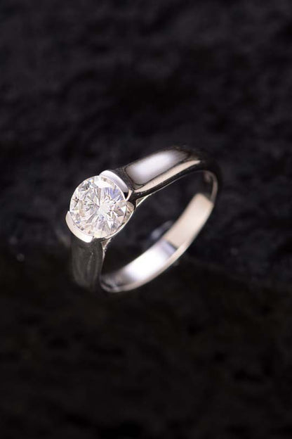 A 1.5 Carat Moissanite 925 Sterling Silver Ring by Marianela's Exclusive Shop, LLC is displayed against a dark, textured background. The moissanite is prominent and sparkling, held by a sleek and simple band made of 925 sterling silver.