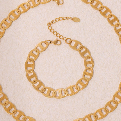 A close-up of the Luxe Gold Chain Bracelet from Marianela's Exclusive Shop on a textured beige surface highlights its sophisticated design. This stainless steel bracelet, plated in 18K gold, features polished, textured links and an adjustable clasp, exuding elegance.