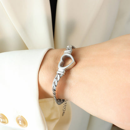 A person wearing a white jacket with gold buttons displays a Titanium Steel Cutout Heart Bracelet from Marianela's Exclusive Shop, LLC on their wrist. The background is off-white and out of focus.