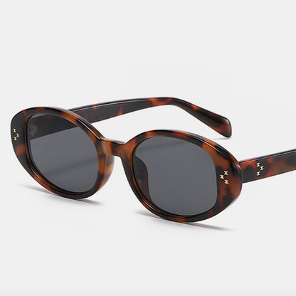 A stylish pair of Polycarbonate Frame Oval Sunglasses from Marianela's Exclusive Shop, LLC featuring tortoiseshell polycarbonate frames with a mottled brown and amber pattern, complete with dark UV400 lenses and small yellow lightning bolt symbols near the hinges on both sides.