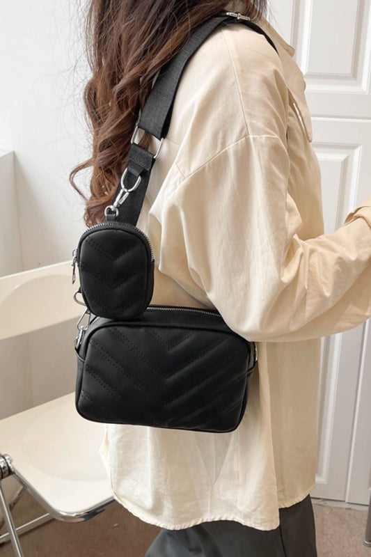 A person with long hair is wearing a cream long-sleeve shirt and a Marianela's Exclusive Shop, LLC Adored PU Leather Shoulder Bag with Small Purse. The bag features a quilted pattern. The person is standing indoors near white furniture and a white wall.