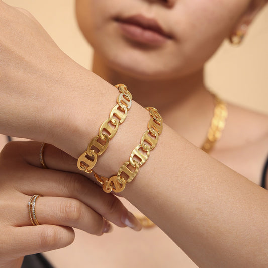 A person showcases the Luxe Gold Chain Bracelet from Marianela's Exclusive Shop on their wrist, beautifully complementing their matching jewelry. The soft, neutral background highlights the bracelet, while they wear a black top.