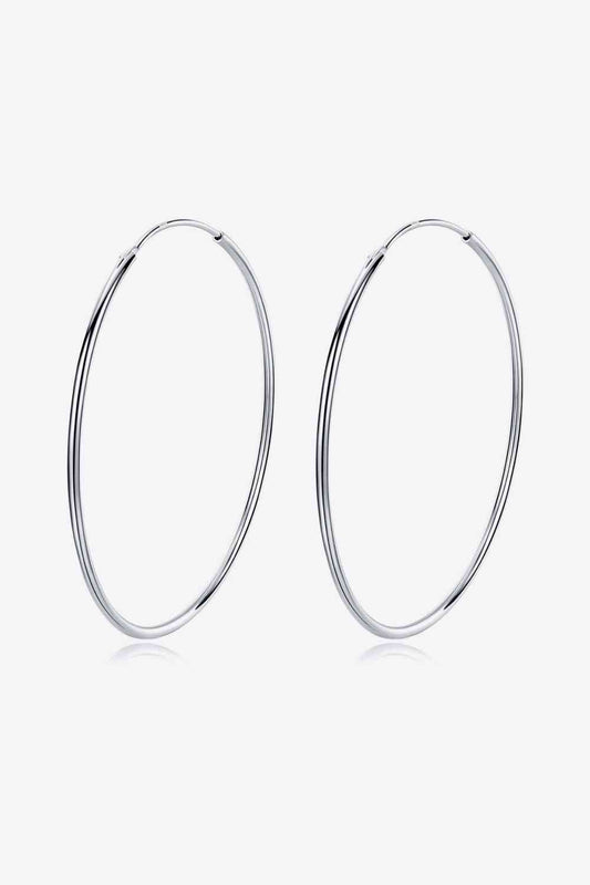 A pair of platinum-plated hoop earrings displayed against a white background. The 925 Sterling Silver Hoop Earrings by Marianela's Exclusive Shop, LLC are large and thin, boasting a simple and elegant design that epitomizes minimalist style.