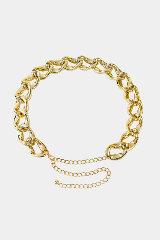 A shiny gold chain belt with large, interlocking links. It features an adjustable clasp with an extender chain and a small dangling charm at the end. This trendy fashion accessory, displayed on a plain white background, boasts bold acrylic links for a modern twist. The Acrylic Curb Chain Belt from Marianela's Exclusive Shop, LLC is perfect for adding a touch of elegance to any outfit.